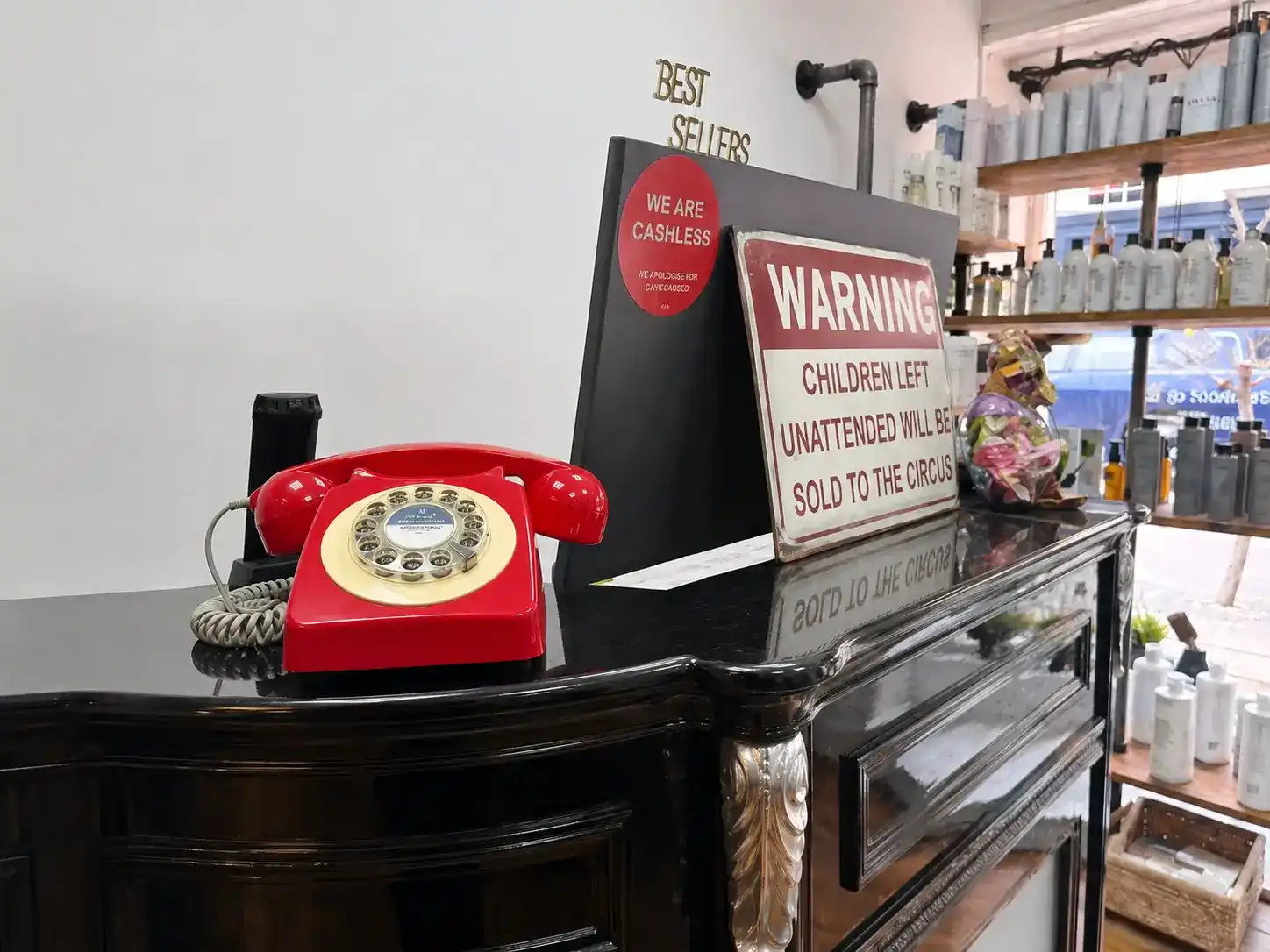 The iconic red 1970s rotary telephone on the Victorian reception desk at The Establishment Hairdressing, Farnham · with the 'children will be sold to the circus' warning sign
